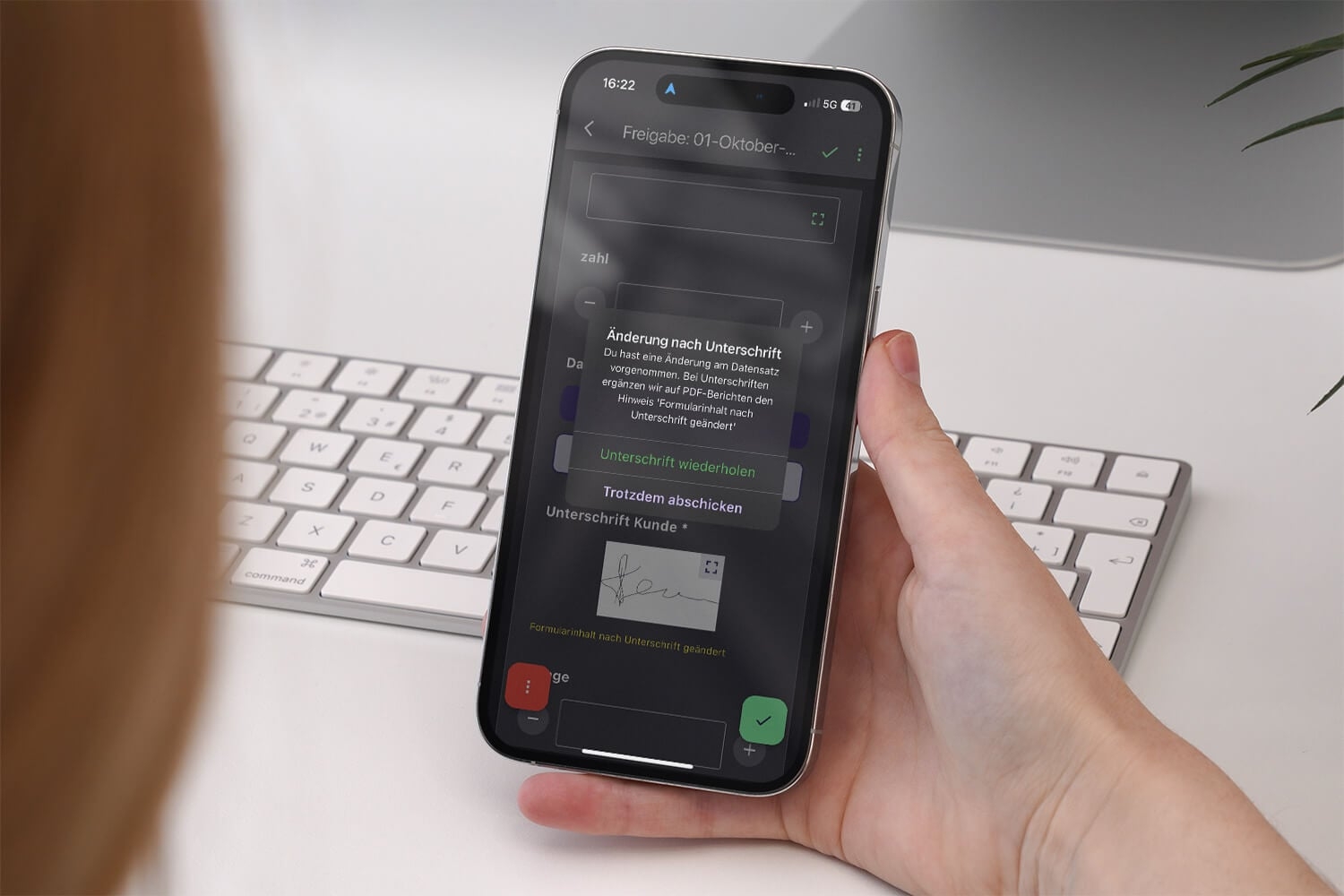 Hand hält ein Smartphone mit einer Freigabe-Aufgabe in der Offpaper App: Ein Dialog weist auf die Änderung nach der Unterschrift hin und bietet Unterschrift wiederholen oder Trotzdem abschicken an